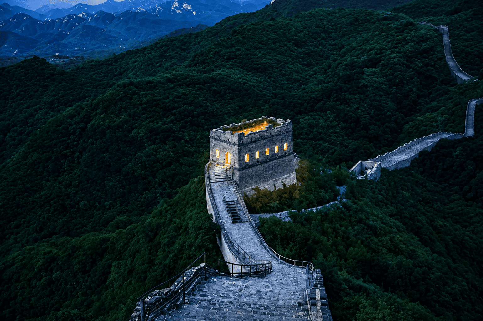 Torre de vigilancia iluminada al anochecer sobre la Gran Muralla China, serpenteando entre montañas boscosas